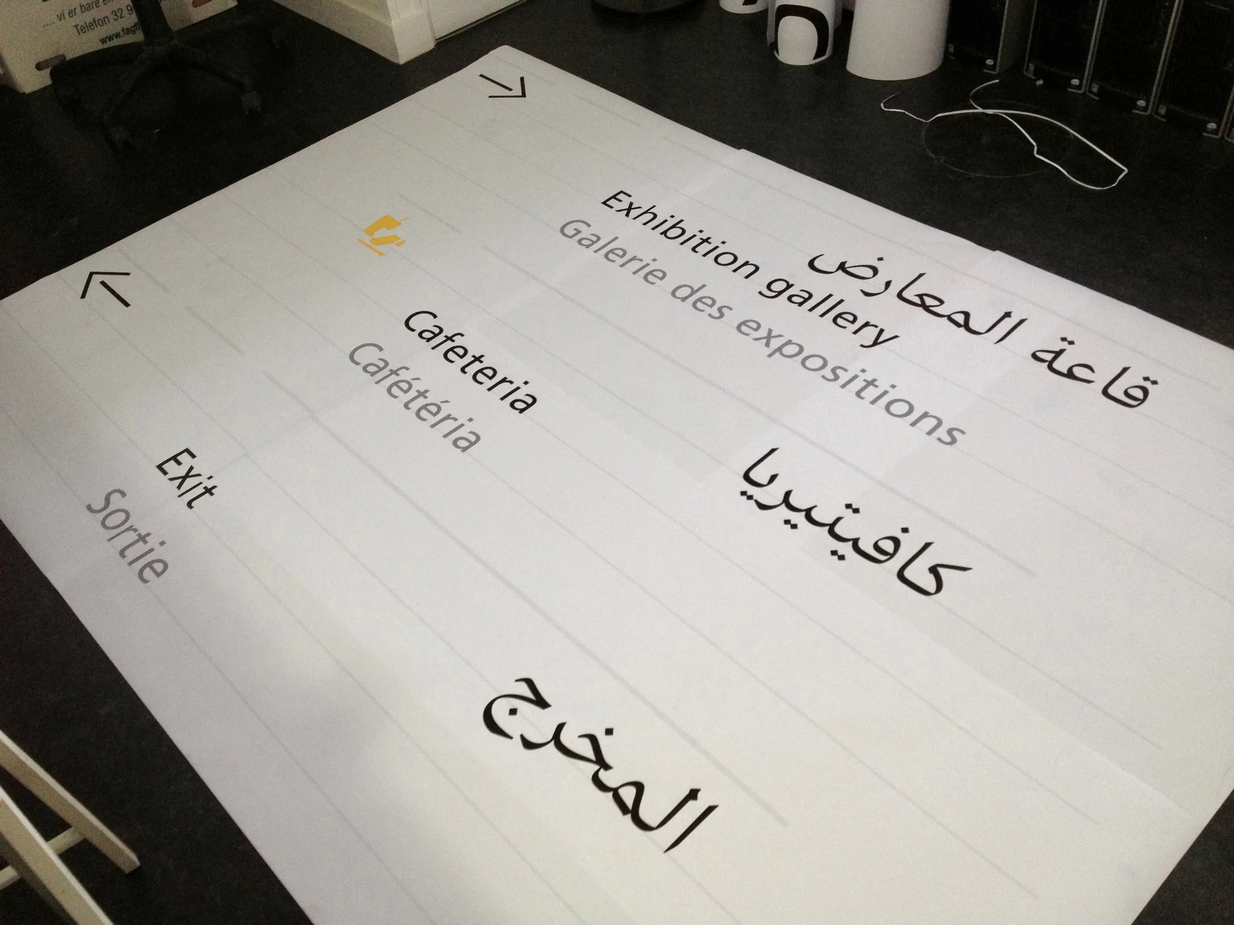 Printed sign layout on a table with English, French and Arabic labels for Exhibition gallery, Cafeteria and Exit