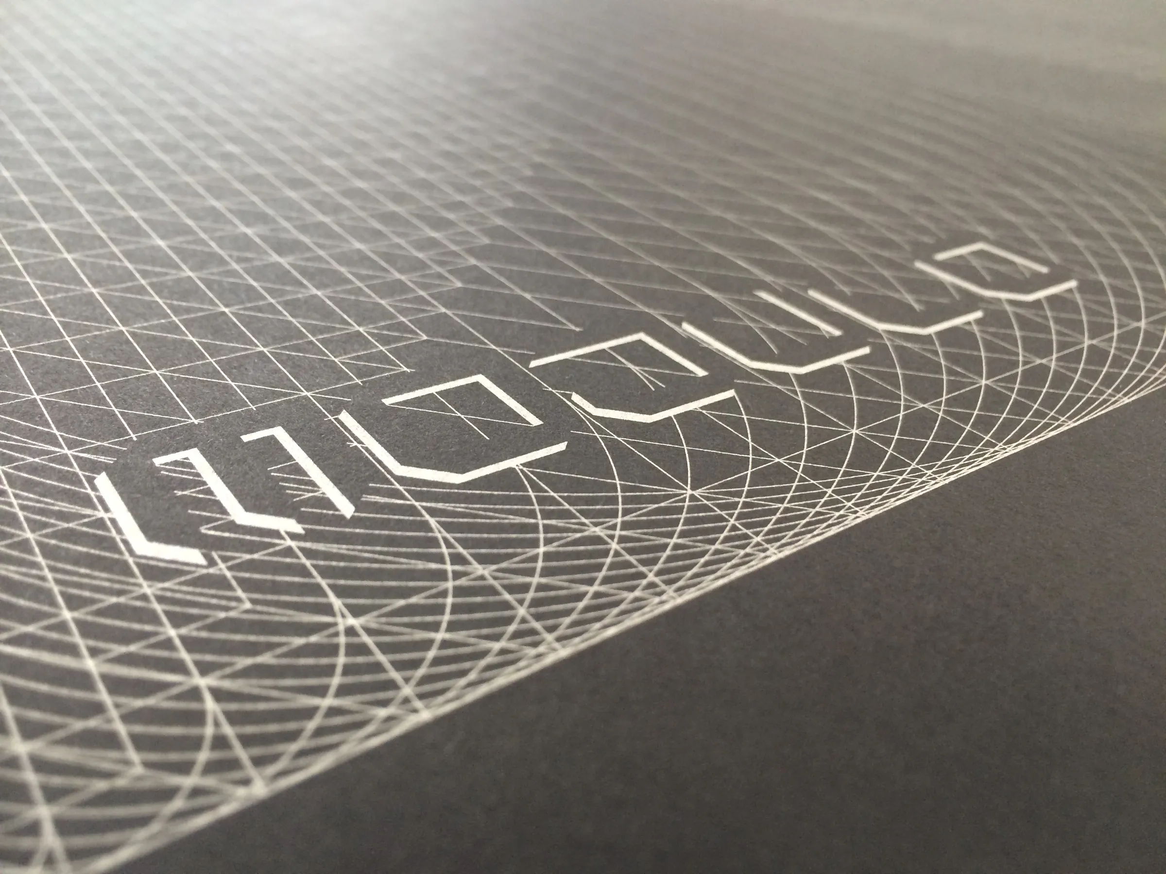 Close-up, at a low angle, of a silver-on-grey print of a construction grid of overlapping lines and arcs, with a row of angular Modulo letterforms outlined within it