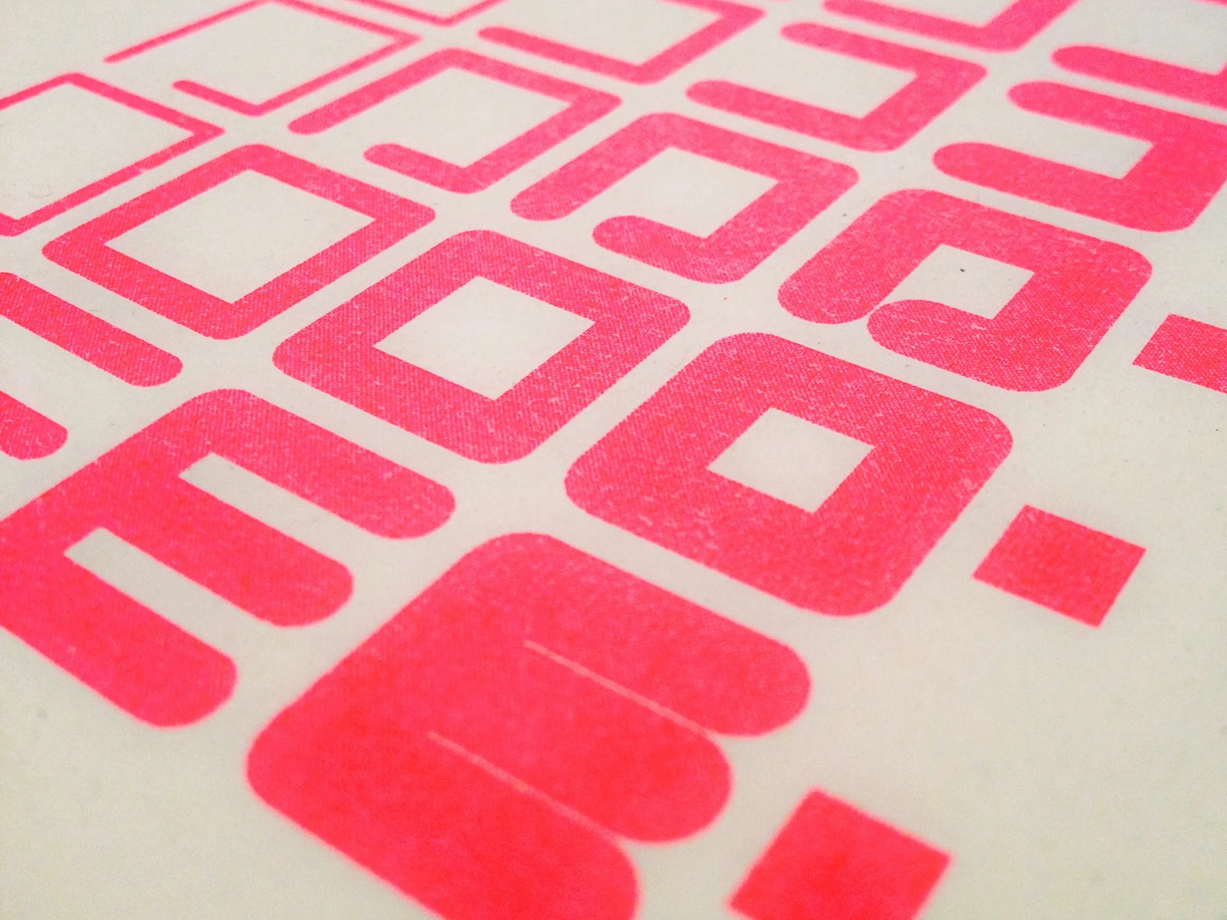 Close-up, at a low angle, of rounded square Modulo letterforms printed in fluorescent pink ink on off-white paper